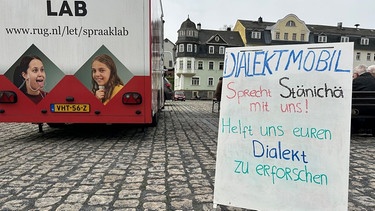 Ein Schild vor einem mobilen Sprachlabor aus den Niederlanden fordert die Bürger im südthüringischen Steinach dazu auf, mit Wissenschaftlern Dialekt zu reden. | Bild: BR/Andi Ebert