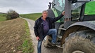 Neben einem grünen Traktor steht Landwirt Hans Steiner auf einer Straße am Feldrand. | Bild: BR/Stefanie Heiß