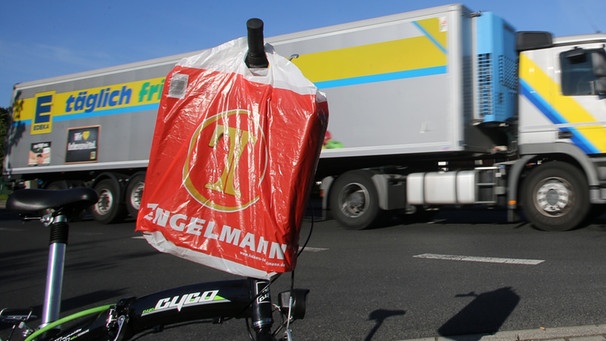 Ein Edeka-Lastwagen fährt in Moers (Nordrhein-Westfalen) zum Edeka-Zentrallager an einem Fahrrad mit einer Tengelmann-Einkaufstüte vorbei.  | Bild: picture-alliance/dpa