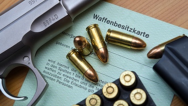 Eine Kaliber 9 mm Pistole, Patronen und ein Magazin liegen auf einer Waffenbesitzkarte. | Bild: pa/dpa/Patrick Pleul