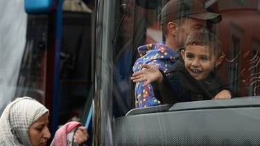 Ein Flüchtlingsjunge winkt am 06.09.2015 vor dem Hauptbahnhof in München (Bayern) Passanten und Unterstützern aus einem Bus zu | Bild: picture-alliance/dpa
