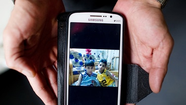 Nadeem (37) aus Latakia in Syrien zeigt am 17.11.2015 in Garmisch-Partenkirchen (Bayern) in einer Erstaufnahmeeinrichtung auf seinem Handy ein Foto seiner beiden zurückgelassenen Söhne im einstigen Wohnzimmer.  | Bild: picture-alliance/dpa