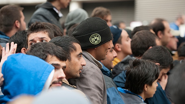 Ein Flüchtling mit einer BVB-Mütze wartet am 23.9.2015 in Berlin mit anderen Flüchtlingen auf dem Gelände des Landesamtes für Gesundheit und Soziales hinter einem Absperrgitter | Bild: dpa-Bildfunk/Paul Zinken