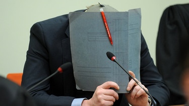 Der Angeklagte Holger G. sitzt am 06.06.2013 im Gerichtssaal des Oberlandesgerichts in München (Bayern) und verbirgt sein Gesicht hinter einer Akte. | Bild: picture-alliance/dpa