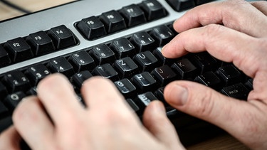Ein Angestellter sitzt in einem Büro an seinem Schreibtisch und tippt auf der Tastatur | Bild: picture-alliance/dpa