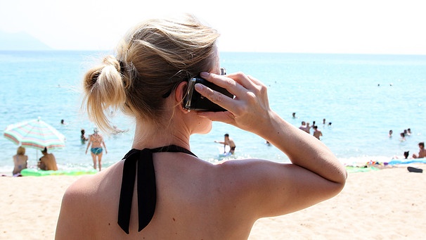 Eine Frau steht mit ihrem Mobiltelefon am Strand und telefoniert | Bild: picture-alliance/dpa/Friso Gentsch