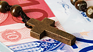 Symbolbild: Rosenkranz mit Holzkreuz auf Geldscheinen | Bild: colourbox.com