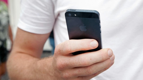 Mann hält ein iPhone von Apple in der Hand. | Bild: picture-alliance/dpa