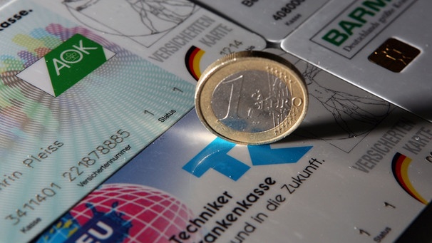 Eine Euromünze auf Versichertenkarten gesetzlicher Krankenversicherungen.  | Bild: picture-alliance/dpa