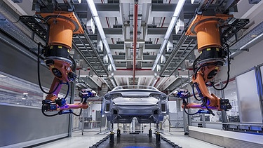 Zwei Roboter fahren auf Schienen an einem Audi entlang | Bild: picture-alliance/dpa