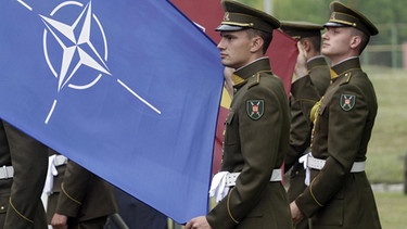 Lithuanian soldiers hold flags during a NATO Force Integration Unit inaugurational event in Vilnius, Lithuania. The Lithuanian command and control centre forms part of six NATO centres - in Bulgaria, Estonia, Latvia, Lithuania, Poland and Romania - are to help on the ground with exercises and planning activities. | Bild: picture-alliance/dpa