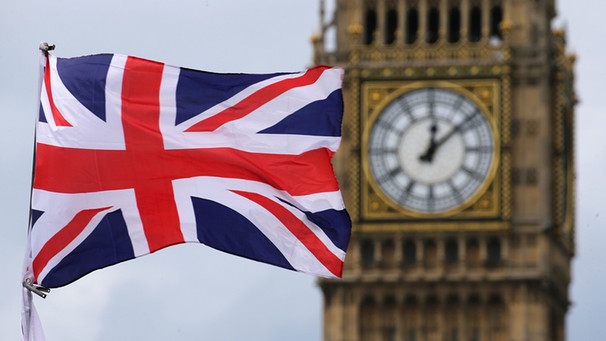 Eine britische Fahne weht in London, Großbritannien, vor dem berühmten Uhrturm Big Ben. Die Uhr auf dem Urm zeigt einige Minuten nach Zwölf an. | Bild: picture-alliance/dpa