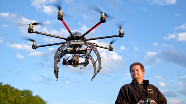 Drohne mit sechs Rotoren, Pilot im Hintergrund | Bild: picture-alliance/dpa | Daniel Karmann