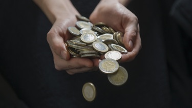 Eine Frau zahlreiche Münzen in den Händen und lässt diese auf den Boden fallen.  | Bild: pa/dpa/Marc Müller