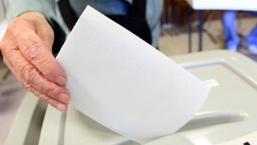 Symbolbild: Ein Stimmzettel wird in eine Wahlurne geworfen | Bild: picture-alliance/dpa