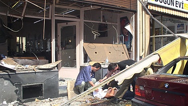 Verletzte werden am 9.06.2004 vor einem durch eine Explosion zerstörten Haus in Köln erstversorgt. Eine mit Nägeln gespickte Bombe war in einem Friseurladen in einem Wohn- und Geschäftsviertel im Stadtteil Mülheim explodiert. | Bild: picture-alliance/dpa