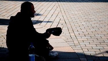 Symbolbild: Ein Bettler sitzt mit einer Mütze in der Hand auf dem Boden.  | Bild: dpa/Friso Gentsch