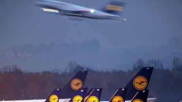 Am Flughafen München stehen Flugzeuge an den Terminals, im Hintergrund startet eine Maschine (Symboldbild). | Bild: picture-alliance/dpa