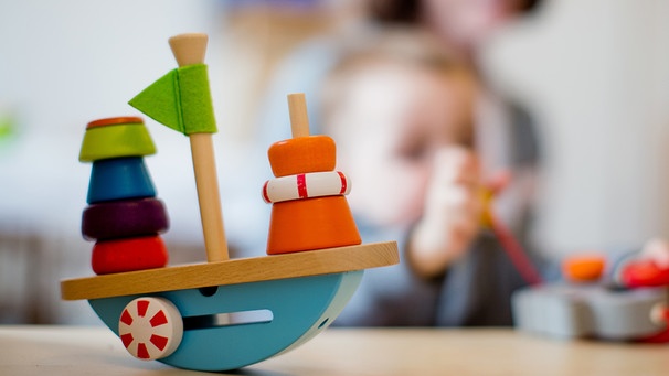 Symbolbild Kita: Holzspielzeug und Kind mit Betreuerin im Hintergrund | Bild: picture-alliance/dpa