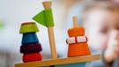 Symbolbild Kita: Holzspielzeug und Kind mit Betreuerin im Hintergrund | Bild: picture-alliance/dpa