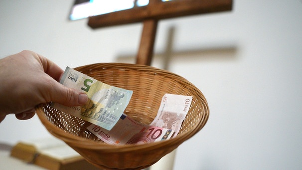 Eine Hand hält einen Sammelkorb mit Geld für die gottesdienstliche Kollekte | Bild: picture-alliance/dpa