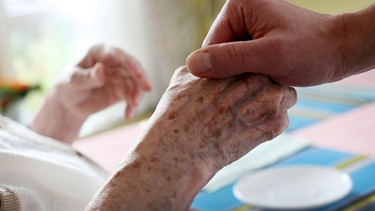 Eine Hand hält die Hand einer Seniorin | Bild: picture-alliance/dpa