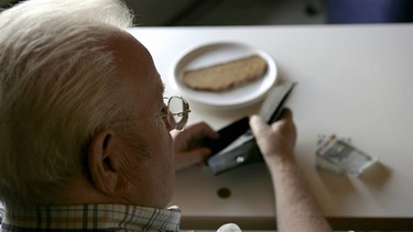 Rentner sieht in eine leere Geldbörse, dahinter eine trockene Scheibe Brot.  | Bild: picture-alliance/dpa/Ulrich Baumgarten