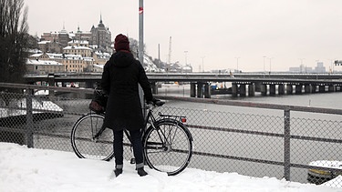 Eine junge Frau schließt ihr Fahrrad im verschneiten Stockholm ab | Bild: picture-alliance/dpa/Britta Pedersen