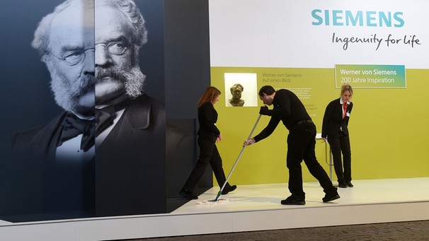 Ein Mann reinigt vor dem Porträt des Unternehmensgründers Werner von Siemens vor Beginn der Siemens-Hauptversammlung in der Olympiahalle den Boden. | Bild: picture-alliance/dpa