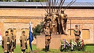 Eine Bronze-Statue, die mehrere bewaffnete Männer zeigt, davor Soldaten und Kränze | Bild: BR/Attila Poth