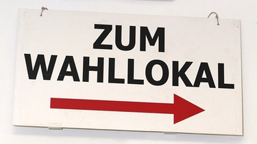 Wegweiser zum Wahllokal, darüber zeigt ein Pfeil in die Gegenrichtung zum Notausgang | Bild: pa/dpa/Ernst Weingarten
