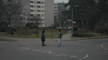 Yussuf (Shadi Eck, rechts) und Elif (Safinaz Sattar) stehen beim Schriftzug auf der Straße. | Bild: BR/TV60Filmproduktion GmbH/Ralf K. Dobrick