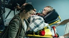 Frank (Michael A. Grimm) wird nach seinem Herzinfarkt ins Krankenhaus gebracht, während Katrin (Eva Meckbach) ihn besorgt begleitet. | Bild: BR/die film gmbh/Hendrik Heiden