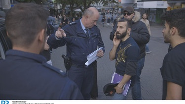 Hassan diskutiert bei einer Aktion in Essen mit der Polizei. | Bild: BR/Till Vielrose/NEOS Film.
