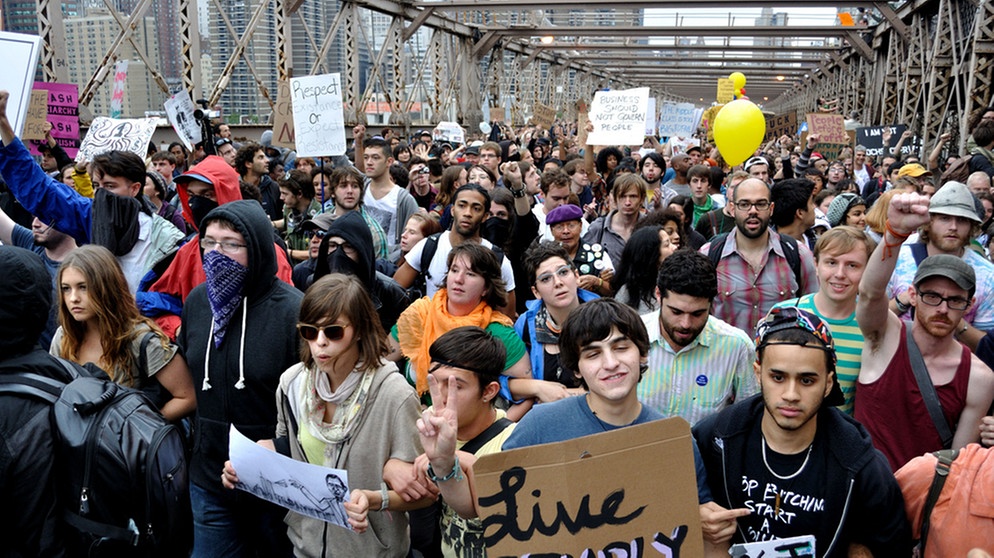Demonstranten am 01.10.2011 auf der Brooklyn Bridge in New York. Bei einer Kundgebung in New York gegen zunehmende Armut und die Macht der Banken hat die Polizei mehr als 700 Demonstranten festgenommen. Das berichtete die Zeitung «New York Times». Zu dem Einsatz am Samstag sei es wegen der Behinderung des Straßenverkehrs auf der Brooklyn Bridge gekommen, sagte Polizeisprecher Paul Browne dem Blatt. Der Demonstrationszug mit rund 1500 Teilnehmern war Teil der Protestaktion «Occupy Wall Street» («Besetzt die Wall Street»), mit der Aktivisten seit zwei Wochen im Finanzdistrikt im Süden Manhattans gegen Ungerechtigkeiten im Wirtschaftssystem protestieren. Foto: Stanley Rogouski dpa | Bild: Stanley Rogouski