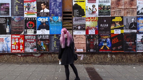 Eine Frau betrachtet eine Wand voller Konzertplakate | Bild: picture-alliance/dpa