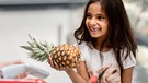 Ein kleines Mädchen freut sich beim Einkaufen über die Ananas in ihrer Hand | Bild: mauritius-images