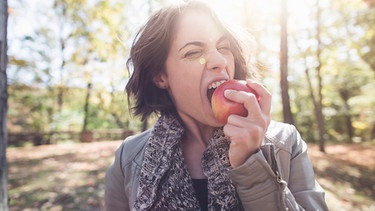 Eine Frau isst einen Apfel in einem Wald | Bild: mauritius images / Image Source / Chad Springer