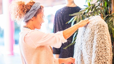 Frau sieht sich in einem Geschäft eine Pelzjacke aus Kunstpelz an. | Bild: mauritius images