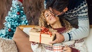 Ein Mann übergibt an eine Frau ein Geschenk und küsst sie dabei auf die Wange. | Bild: mauritius images / Fabio and Simona