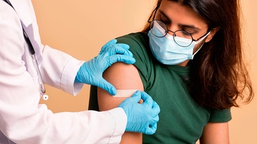 Ärztin klebt Pflaster auf den Arm eines Patienten nach einer Impfung | Bild: mauritius images / Prostock-studio / Alamy / Alamy Stock Photos