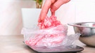 Eine Hand greift nach eingefrorenem Hackfleisch, dass in einer Plastiktüte auf einer Küchenwaage liegt. | Bild: mauritius images / Olga Vorobeva / Alamy / Alamy Stock Photos