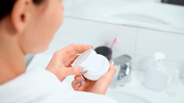 Frau hält im Badezimmer eines Hotels eine Creme-Probe in de Händen | Bild: mauritius images