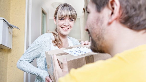 Paketbote übergibt einer Frau ein Paket an der Wohnungstür | Bild: mauritius images