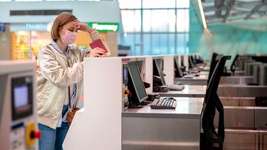 Frau steht mit Reisepass an einem Flughafenschalter | Bild: mauritius images
