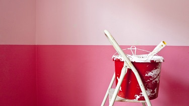 Ein Eimer Farbe steht auf einer Stehleiter vor einer rosa-fuchsia farbenen Wand. | Bild: mauritius images / STOCK4B