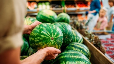 Ein Arm greift in einem Supermarkt nach einer Wassermelone | Bild: mauritius-images