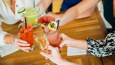 Drinks werden in der Mitte des Tisches zusammengestoßen | Bild: mauritius images / Blend Images / Inti St Clair