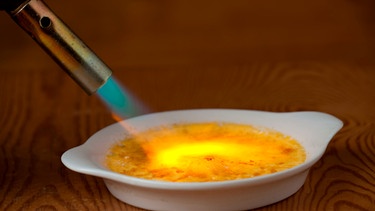 Flamme eines Bunsenbrenners karamellisiert die Zuckerschicht auf einer Crème Brûlée. | Bild: mauritius images / Zoonar GmbH / Alamy / Alamy Stock Photos
