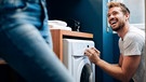 Ein Mann belädt eine Waschmaschine | Bild: mauritius images / Westend61 / Sofie Delauw